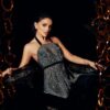 Gorgeous female with makeup wearing fancy dress with long hem looking at camera while standing near round decorative elements in room